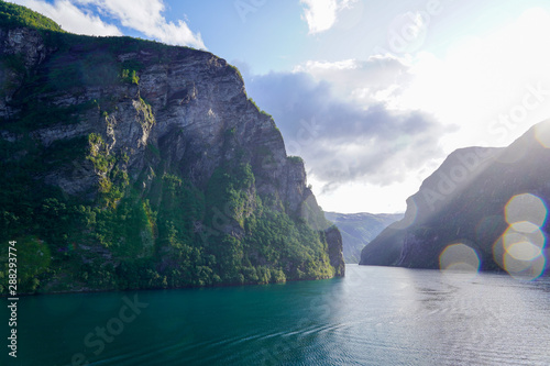 Geiranger (Norwegen) , Die Unberührte Natur der Norwegischen Fjorde , Beauty of Norway mit See und Sicht auf Felsen bei blauem Himmel mit kleinen Norwegischen Häusern 