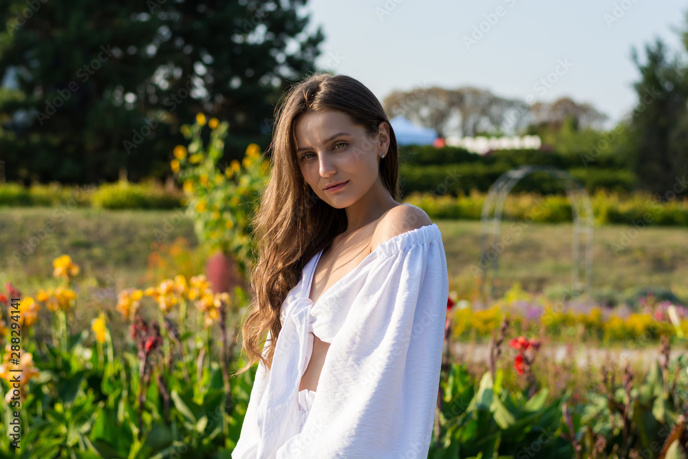 Young beautiful woman with bare shoulders in white clothes in the park at the sunset Young beautiful woman with bare shoulders in white clothes in the park at the sunset