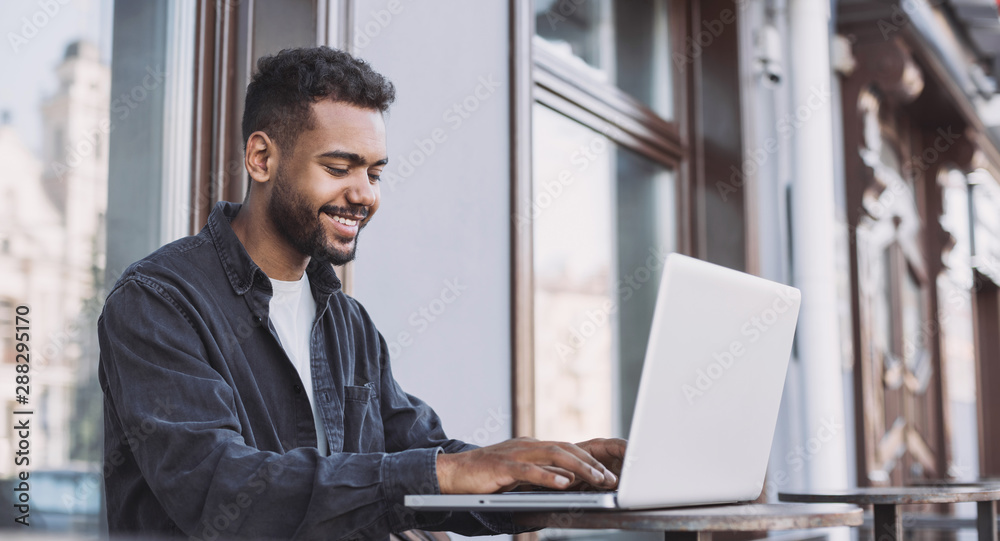 Smiling man student using laptop computer in a city. Young handsome men having coffee break. Modern lifestyle, connection, business, freelance work concept