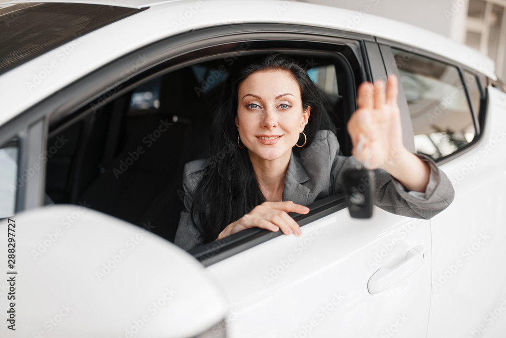 Happy woman shows key to the new car in showroom