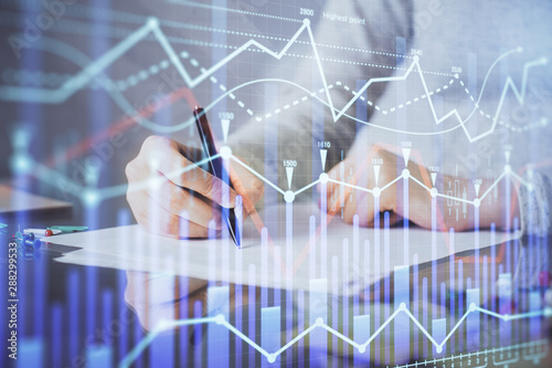 Hand taking notes in notepad. Forex chart holograms in front. Concept of research. Multi exposure