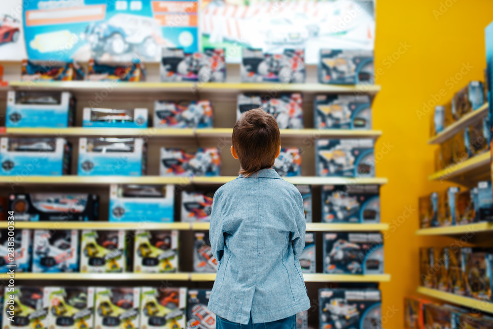 Little boy at the shelf in kids store, back view - obrazy, fototapety, plakaty 