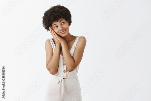 Everytime thinking about boyfriend before sleep. Tender sensual and cute African American girlfriend with gray overalls, leaning head on palms as if lying on bed and dreaming with gentle smile photo