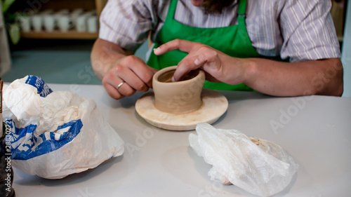 A raw clay pot in the hands of a potter. Workshop in the pottery workshop. Clay pot on a potter`s wheel