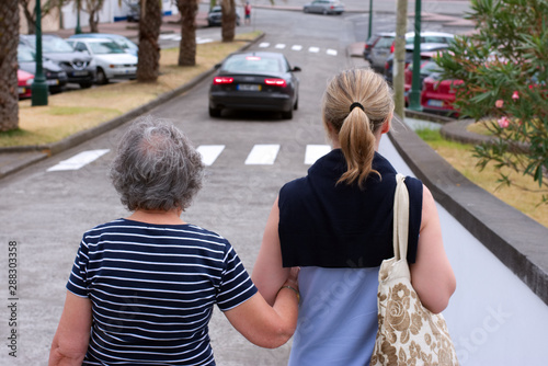 Younger daughter helps old mother down the street
