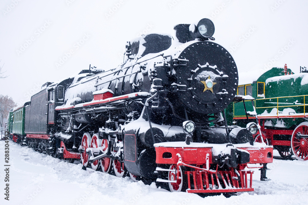 Fototapeta premium Steam train in snow. Soviet black and red locomotive. Steam engine transport.