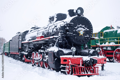 Steam train in snow. Soviet black and red locomotive. Steam engine transport.