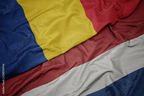 waving colorful flag of netherlands and national flag of romania.
