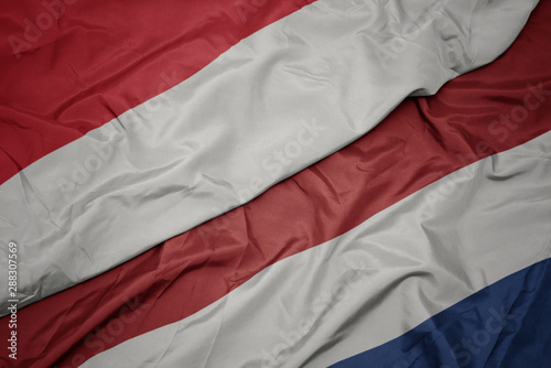 waving colorful flag of netherlands and national flag of indonesia.