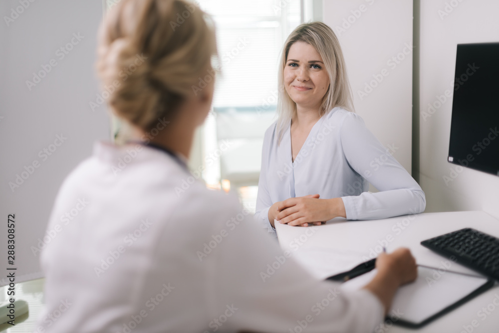 Healthcare and medical concept - doctor with young woman patient in hospital, at doctor appointment. Therapist female sitting at table and asks the patient questions