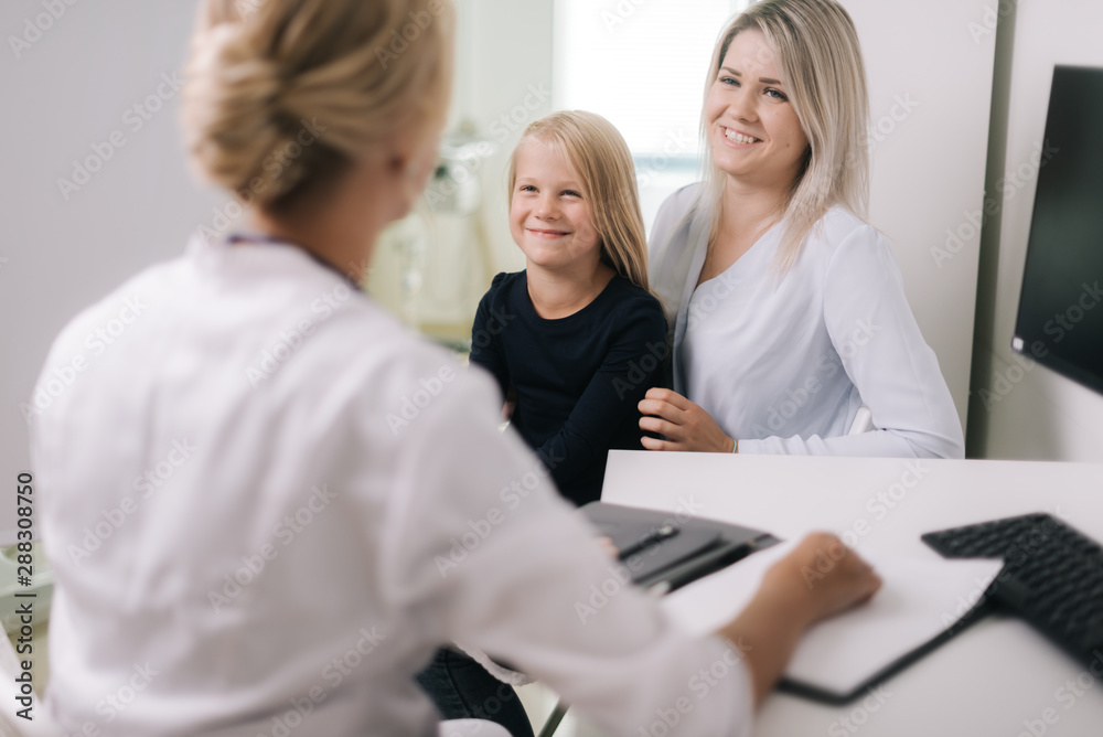 Fototapeta premium Little girl with blond hair with her mother at a doctor on consultation. Mother holding baby in her hands.