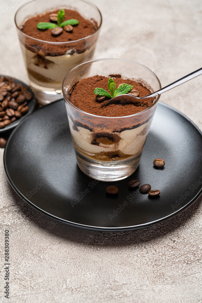 Portion of Classic tiramisu dessert in a glass cup on concrete background Portion of Classic tiramisu dessert in a glass cup on concrete background