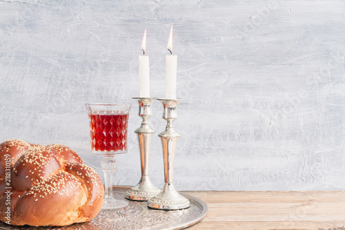 Shabbat or Sabbath kiddush ceremony composition with a traditional sweet fresh loaf of challah bread, glass of red kosher wine and candles on a vintage wood table with copy space