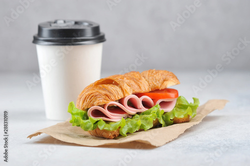 Coffee in a white paper cup and a ham sandwich. Coffee to go concept. Light background. Close-up. Negative space.