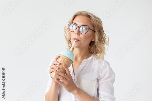 Cute charming young woman is drinking a cocktail from a straw posing against a white background.