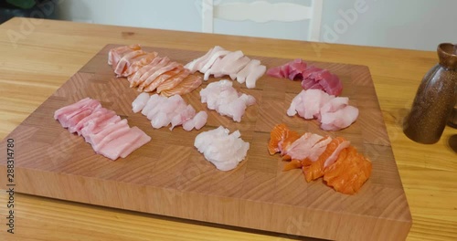 Slow pan around a beautiful presentation of fresh sliced sashimi fish on a wooden board sitting in the middle of wooden table next to a sake bottle and cups. Fish includes raw tuna, salmon and snapper photo