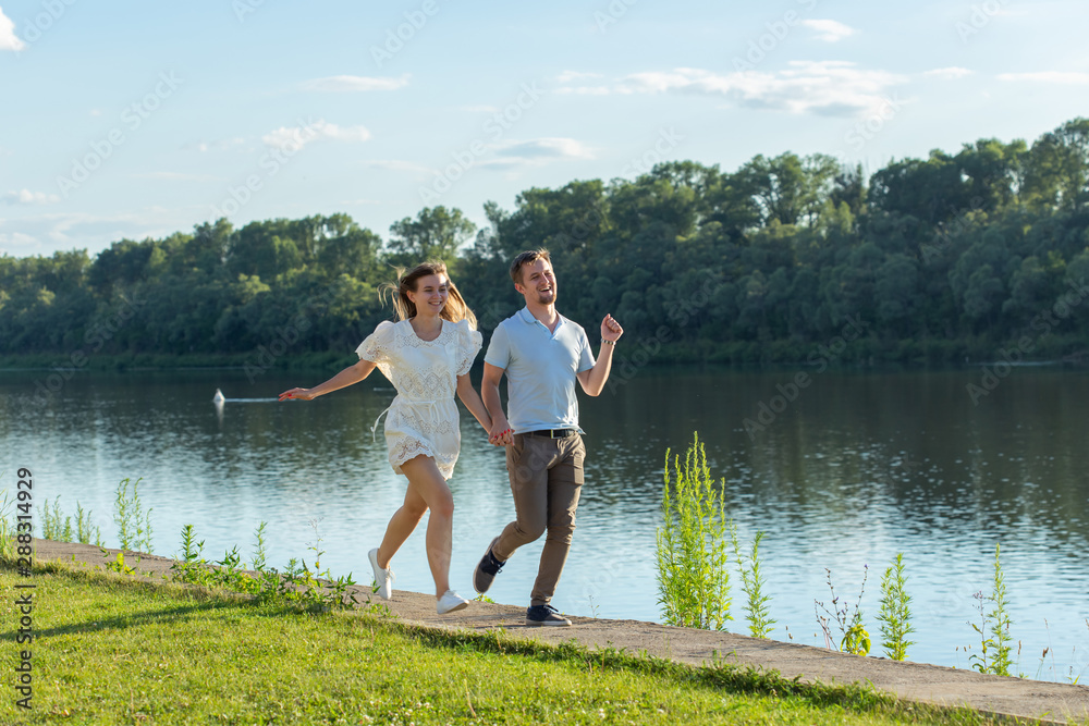 Love and relationship concept - The happy man and woman running in a park near a lake Love and relationship concept - The happy man and woman running in a park near a lake