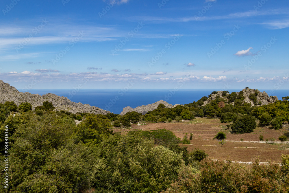 Scenic view at landscape of Serra de Tramuntana on island Mallorca, Spain on a sunny day with rocks in front and mediterranean sea in background Scenic view at landscape of Serra de Tramuntana on island Mallorca, Spain on a sunny day with rocks in front and mediterranean sea in background