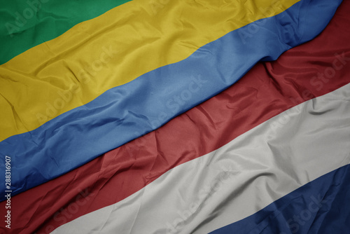 waving colorful flag of netherlands and national flag of gabon.