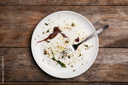 Dirty plate with food leftovers and fork on wooden background, top view