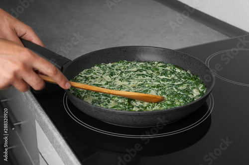 Woman cooking tasty spinach dip on kitchen stove, closeup view