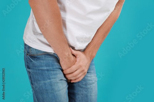 Man suffering from pain on turquoise background, closeup. Urology problems