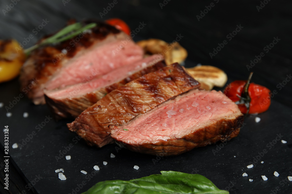 Grilled meat served with garnish on slate plate, closeup