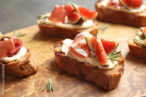 Bruschettas with cream cheese, prosciutto and figs served on wooden board, closeup