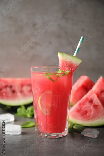 Glass of tasty refreshing drink with watermelon on grey table