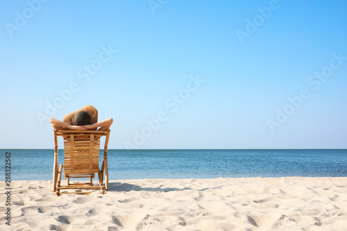 Fotografering Young woman relaxing in deck chair on sandy beach