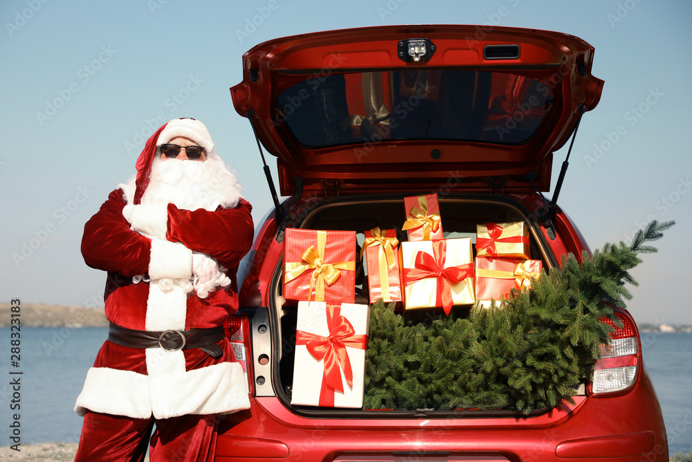Authentic Santa Claus near car with open trunk full of presents and fir tree outdoors - obrazy, fototapety, plakaty 