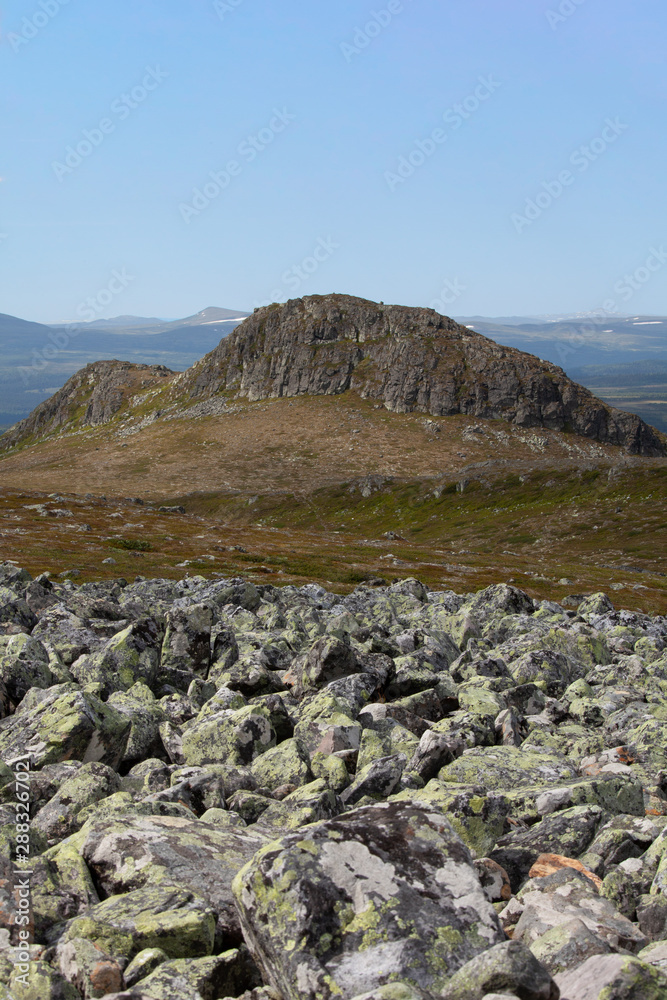 A field with stones in the foreground and a mountain peak in the background under a clear blue sky without a single cloud.