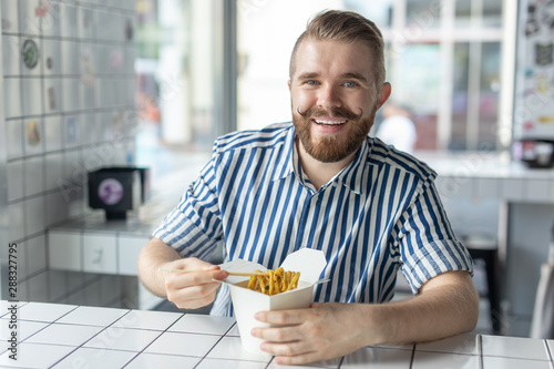 Positive young stylish guy eating chinese noodles in a cafe during a break at work. The concept of rest and healthy snack.