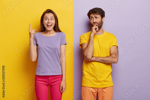 Happy European dark haired woman points index finger above, dressed in casual...