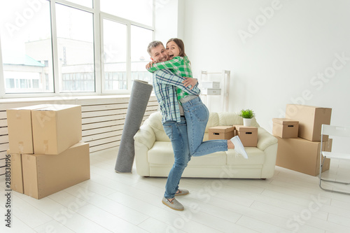 Young couple in denim pants embracing rejoicing in their new apartment during the move. The concept of housewarming and credit for new housing. © satura_