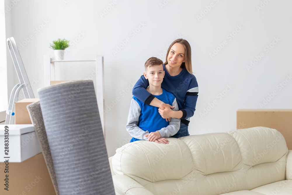 Positive smiling single mother and charming son are posing standing in a new bright comfortable apartment. The concept of moving and mortgages for new housing.