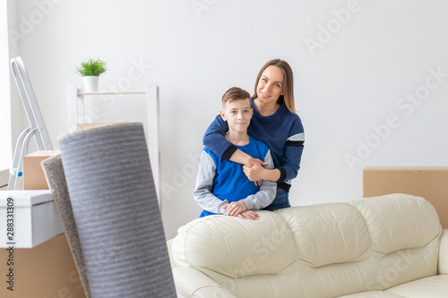 Positive smiling single mother and charming son are posing standing in a new bright comfortable apartment. The concept of moving and mortgages for new housing.