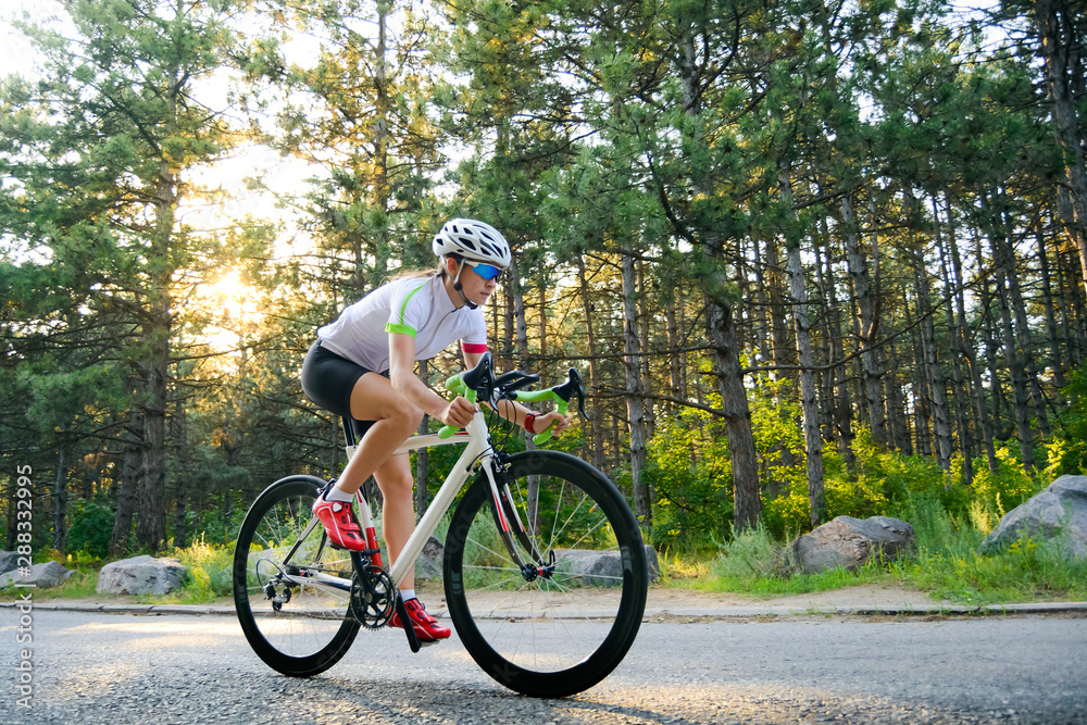 Naklejka premium Young Woman Cyclist Riding Road Bicycle on the Free Road in the Forest at Hot Summer Day. Healthy Lifestyle Concept.