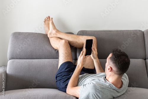 Man lying upside down on the couch reading message.
