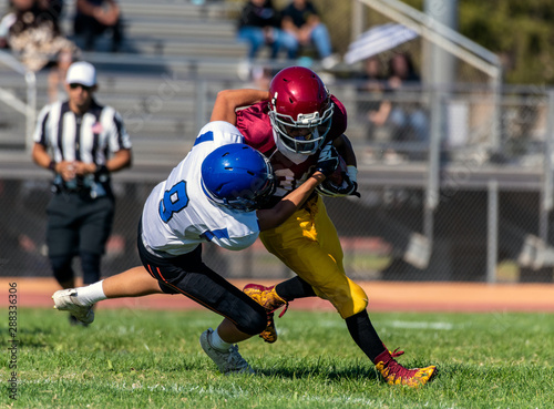 Defensive player number eight has offensive running back with ball wrapped up in his grasp as he attempts to tackle the player during a game.