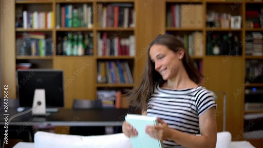 Portrait of pretty beautiful young woman dancing happily at home near a bookshelf. Modern student girl dancing throwing a book in modern house living room. End of school, vacations. Portrait of pretty beautiful young woman dancing happily at home near a bookshelf. Modern student girl dancing throwing a book in modern house living room. End of school, vacations.