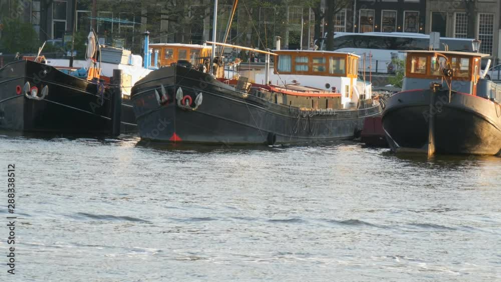 Amsterdam, Netherlands - April 21, 2019: Tourists sail by boat along the Amsterdam canal on which moored boats. Authentic Dutch houses and streets of the capital of the Netherlands Amsterdam, Netherlands - April 21, 2019: Tourists sail by boat along the Amsterdam canal on which moored boats. Authentic Dutch houses and streets of the capital of the Netherlands