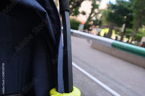 Blue visible part of a stroller with an attached toy with a View to a park with a white and green barrier in the background