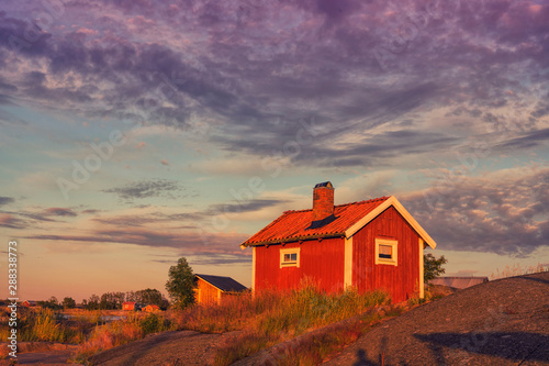 Traditional red wooden house in the island with bridge at sunset clouds sky in Sweden