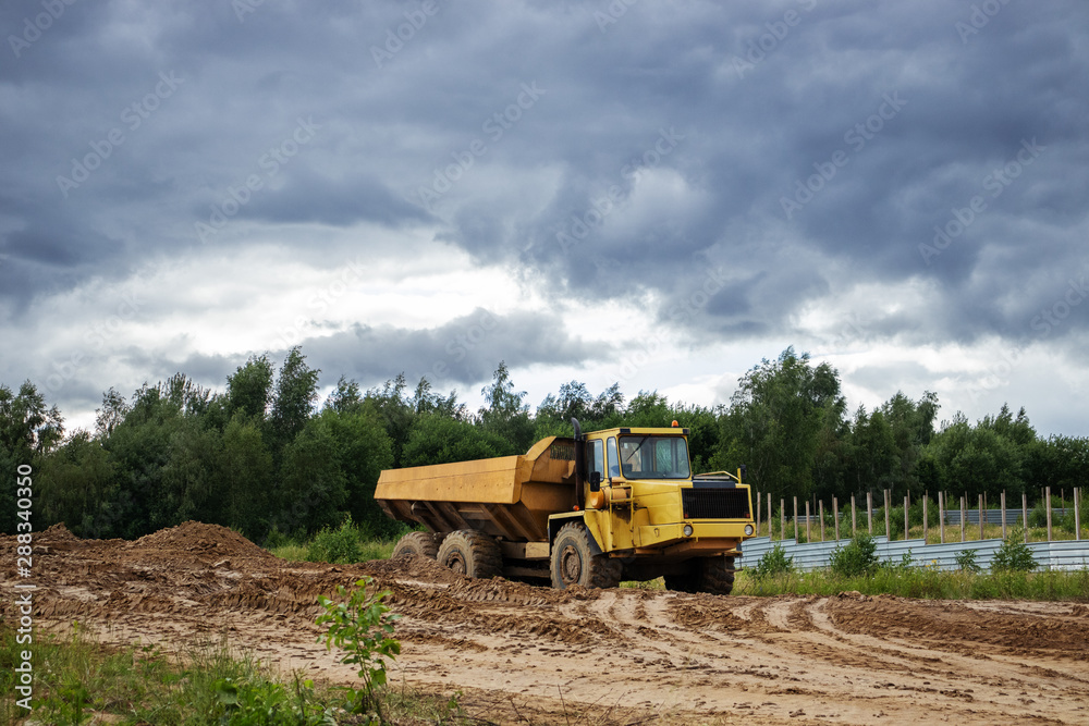 Obraz premium construction site with dump, truck, tree, cloudy sky