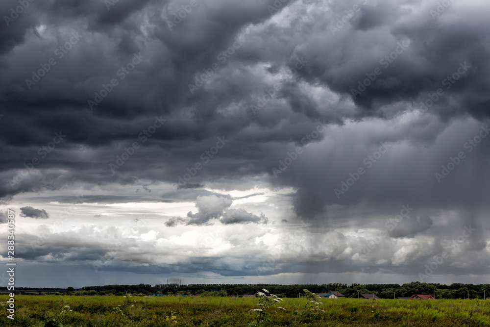 Dark cumulonimbus clouds, with rain coming on the horizon, over a wild field. Sky pattern. Dark cumulonimbus clouds, with rain coming on the horizon, over a wild field. Sky pattern.