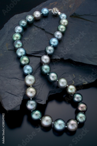 A single strand neclace of large muti colore Tahitian pearls drape over a black slate background. photo