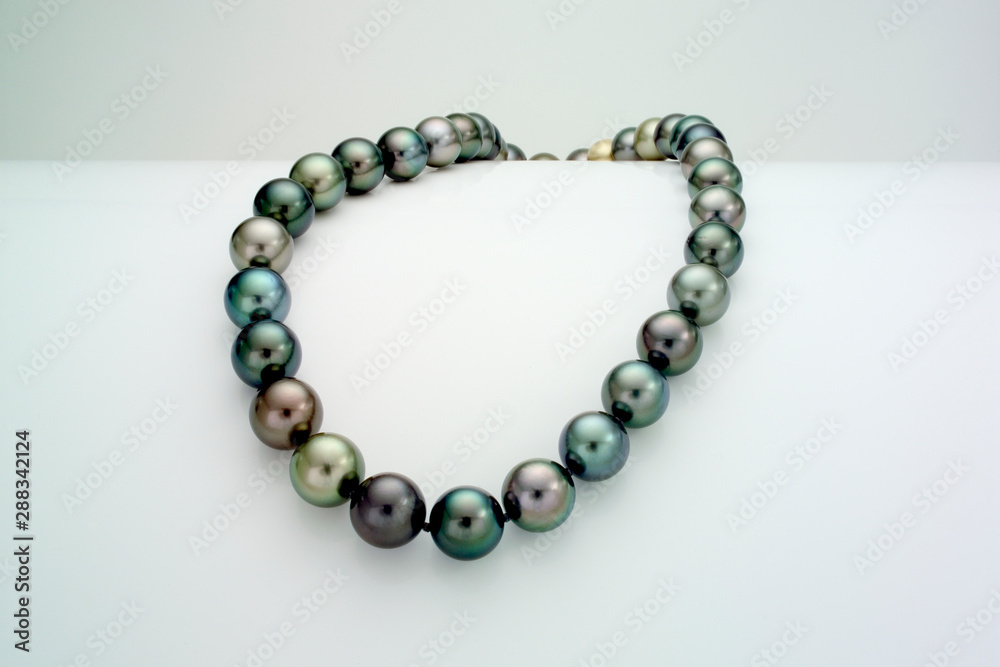 A necklace of a single strand of Tahitian pearls is laid over a curve white surface. A necklace of a single strand of Tahitian pearls is laid over a curve white surface.