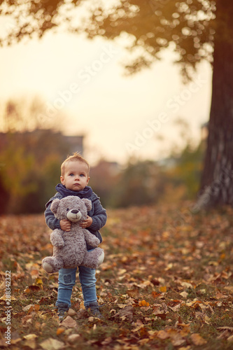 cheerful boy with teddy bear in park on autumn day.