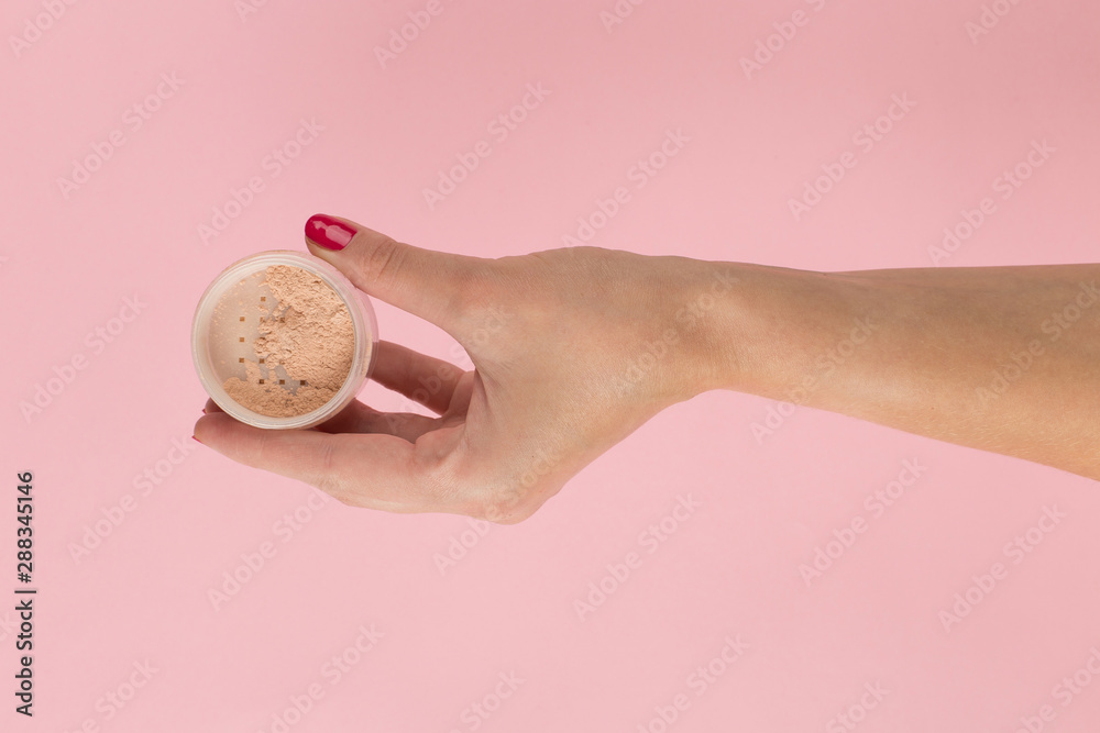 Fototapeta premium Girl hand holds powder from on a pink background. Makeup artist concept, copy space.